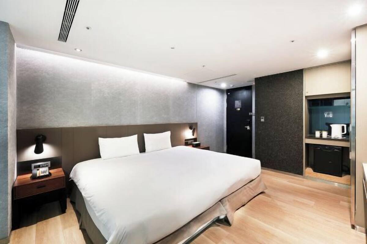 Una habitación de hotel moderna con una cama grande, mesitas de noche, un escritorio integrado y un mini bar.