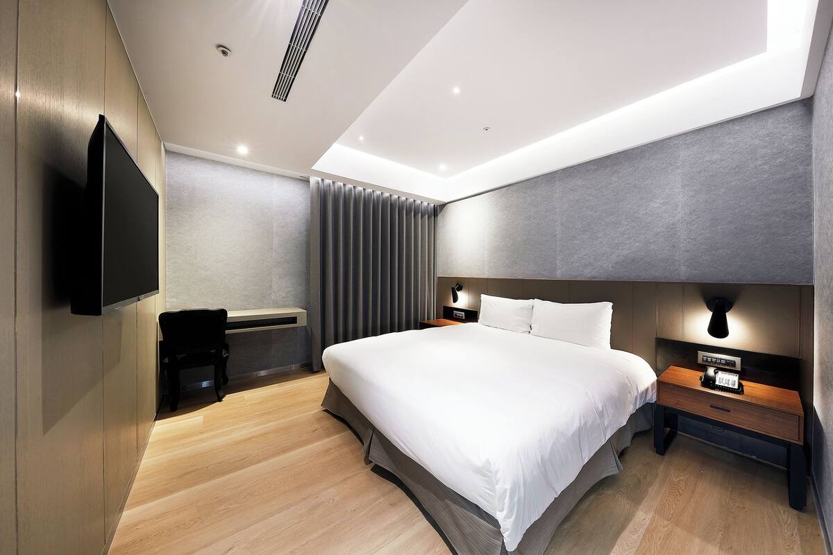 Una habitación de hotel moderna con una cama grande, mesitas de noche, un televisor de pantalla plana y una lámpara de techo.