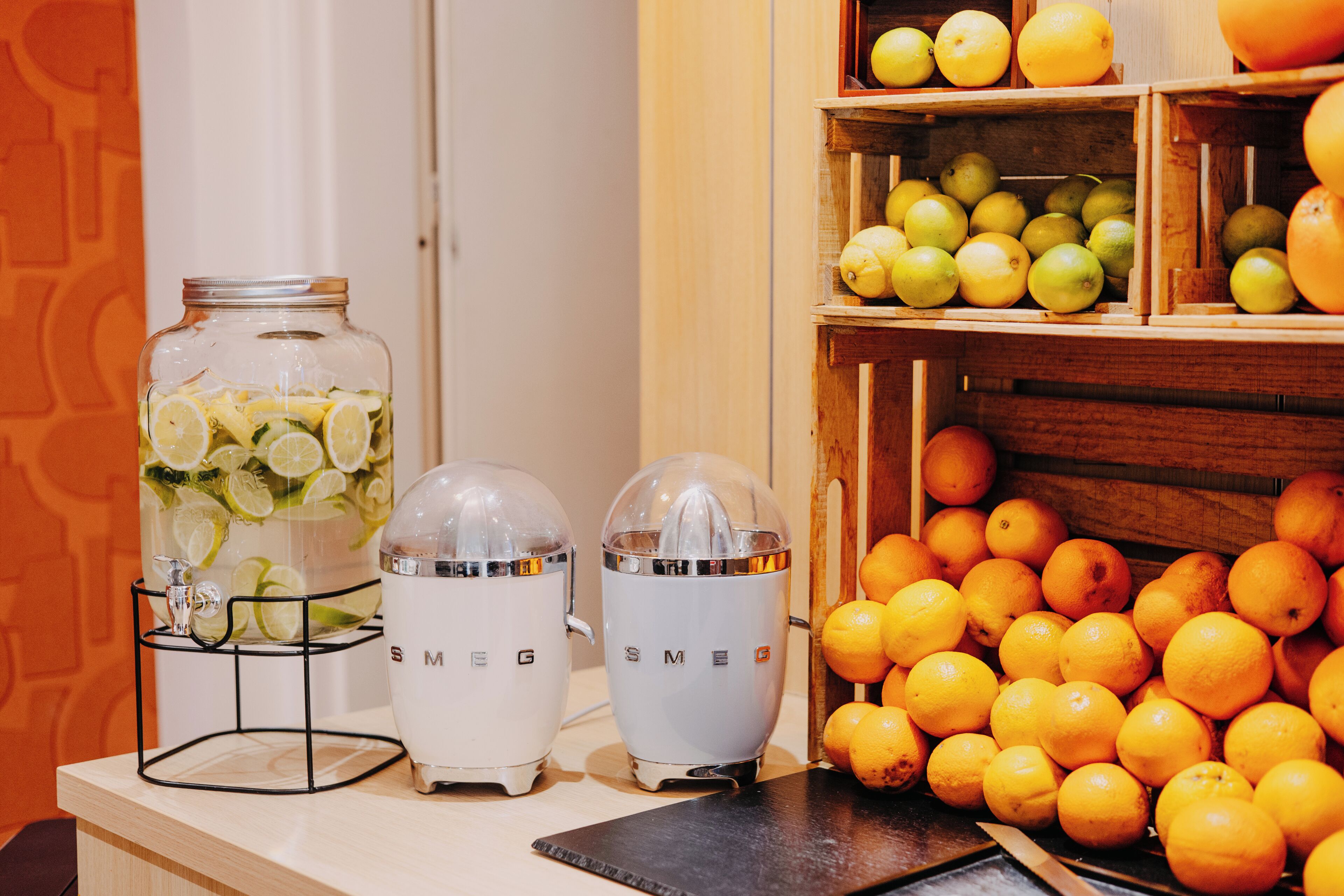 A kitchen counter with two kitchen appliances, a glass jar with citrus slices, and a wooden crate with oranges.