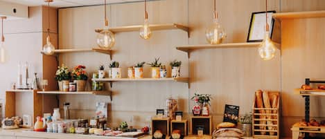 Interno di un caffè con scaffali in legno, lampadine a sospensione e diversi prodotti alimentari.