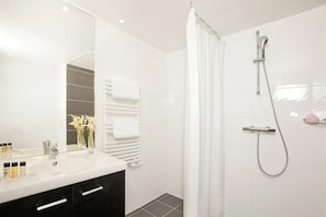 Bathroom features a shower with a handheld showerhead and a curtain, a white vanity, and a large mirror.