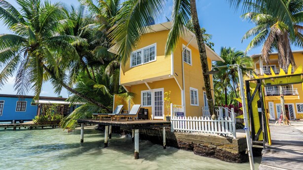 A yellow building with a white fence, a wooden deck, and palm trees. - El Faro del Colibri (Bocas del Toro)