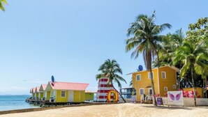A beach with colorful buildings, palm trees, and a clear sky. - El Faro del Colibri (Bocas del Toro)