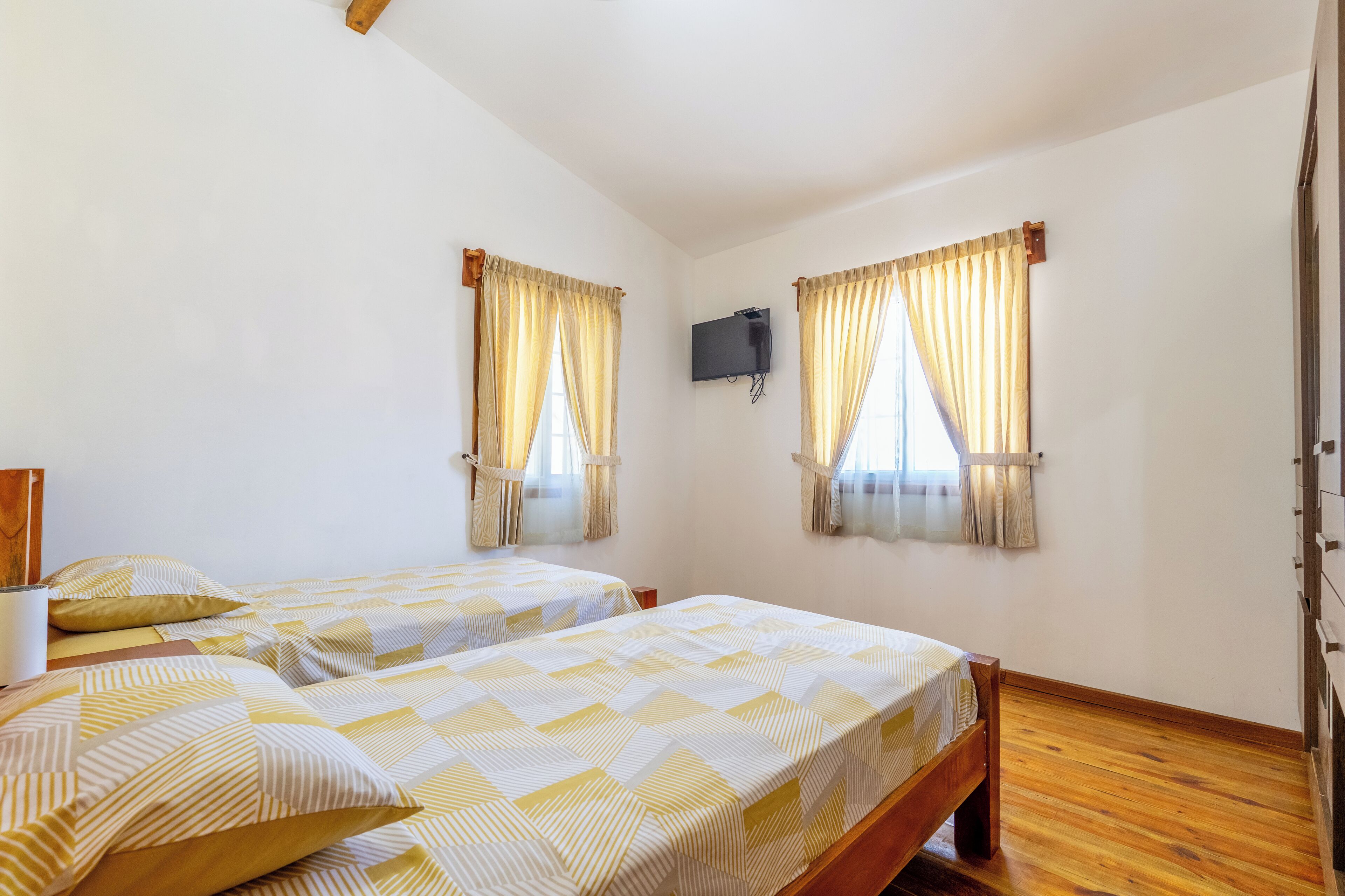 Habitación con dos camas, suelo de madera, televisión de pantalla plana y ventana con cortinas.