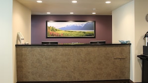 Un comptoir d’accueil avec un téléviseur fixé au mur diffusant des images de paysages, un petit espace d’accueil avec un comptoir, et une horloge murale.