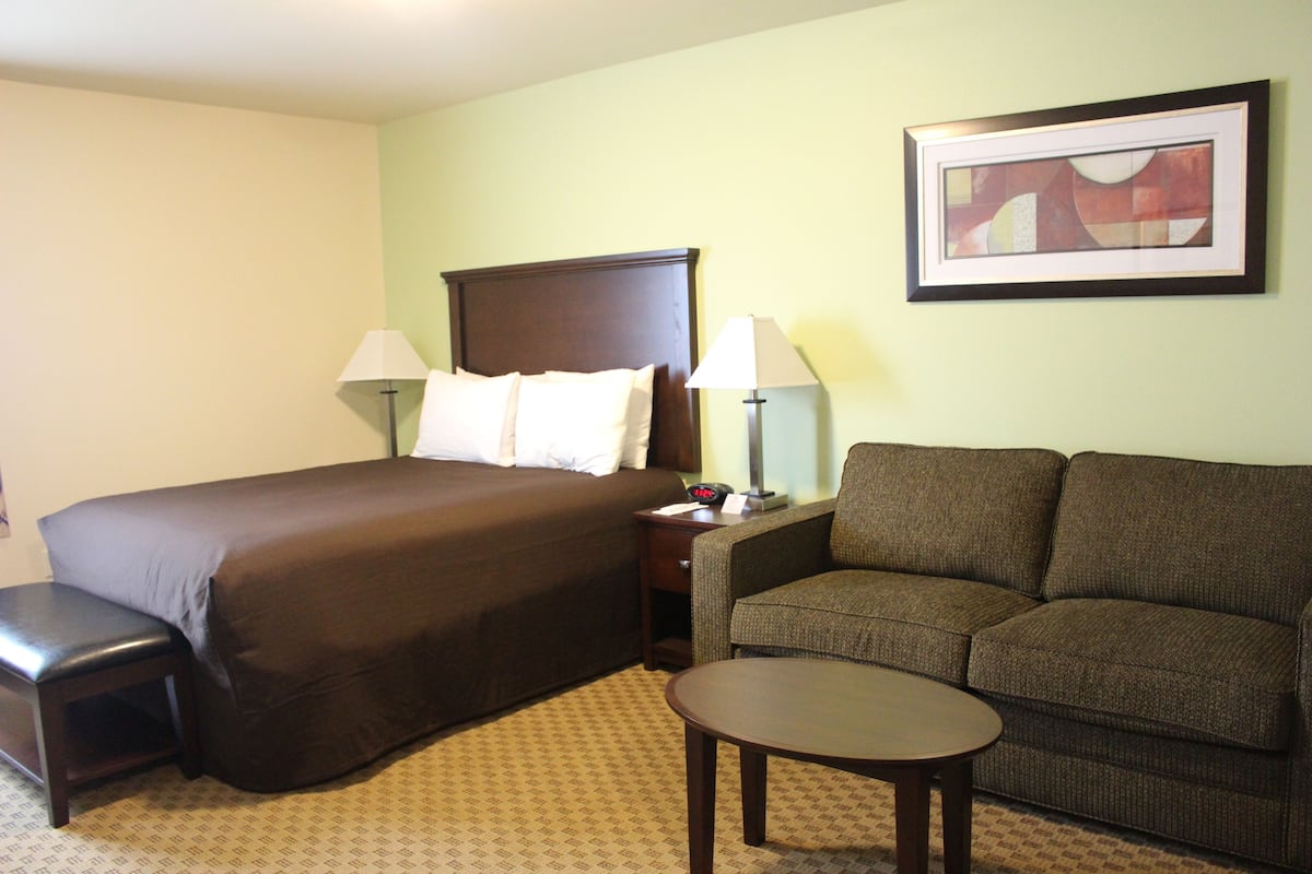 A hotel room with a large bed, a sofa, a small table, and a nightstand with lamps.