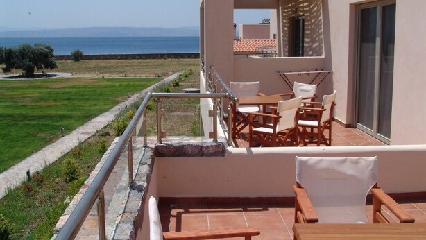 A balcony with a view of the sea, outdoor furniture, and a building with a tiled roof. - Enalia Gi (Mantoudi-Limni-Agia Anna)