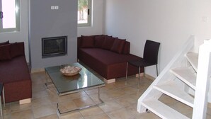 A modern living room with a glass coffee table, a red sofa, a black chair, and a white staircase. - Enalia Gi (Mantoudi-Limni-Agia Anna)