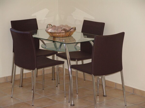 Un comedor con una mesa de vidrio rodeada por cuatro sillas con patas metálicas.