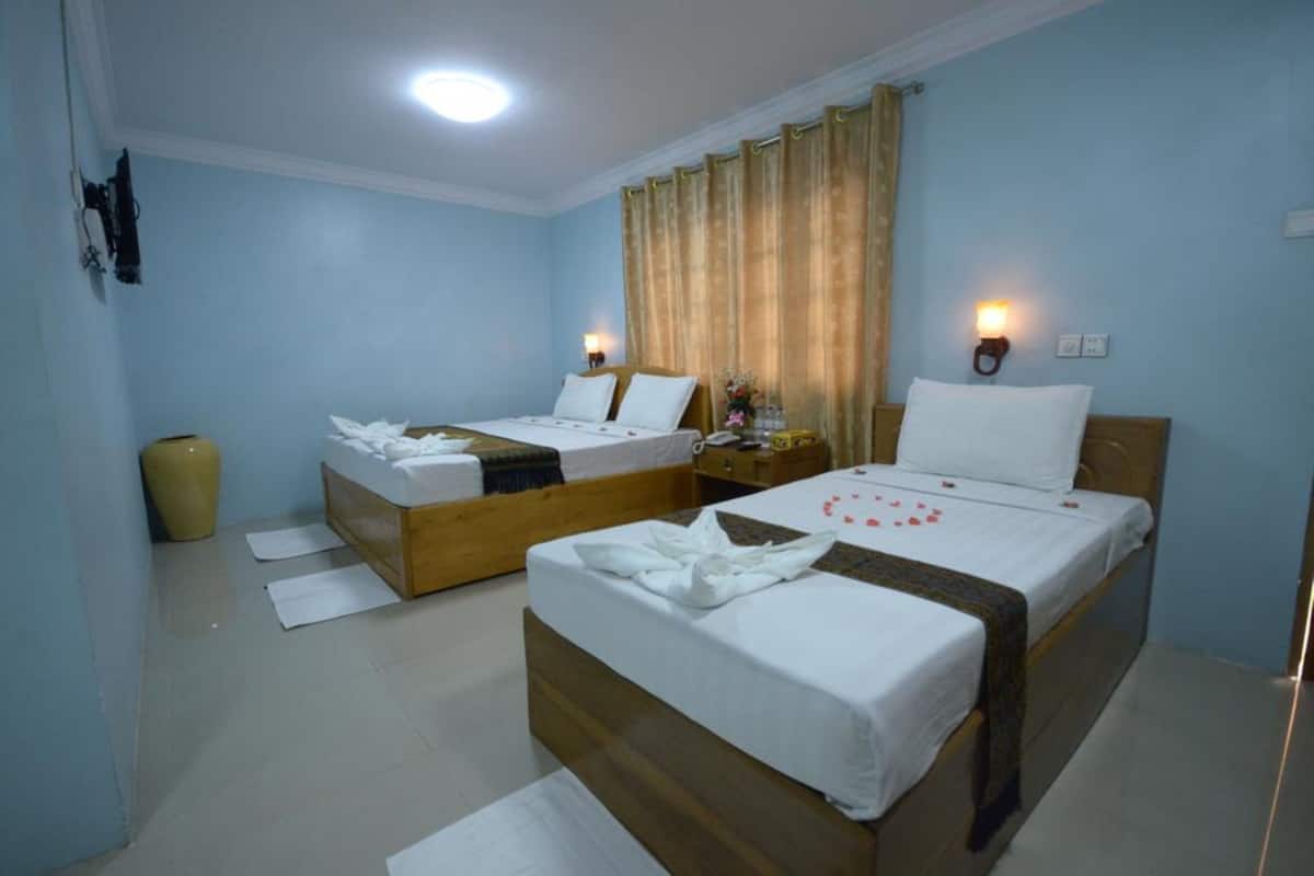 A hotel room with two single beds, a wooden headboard, a bedside table with a lamp, and a large window with curtains.