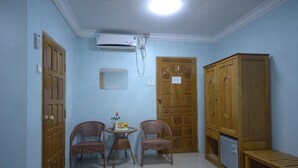 A room with two wicker chairs, a small table with a box and a flower, a wooden wardrobe, a bench, and a wall-mounted air conditioner. - Inlay Palace Hotel (Nyaungshwe)