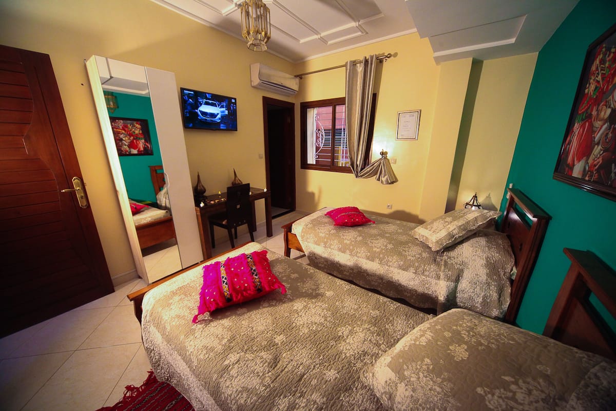 Een hotelkamer met twee bedden, een televisie, een airconditioningsunit en een bureau.