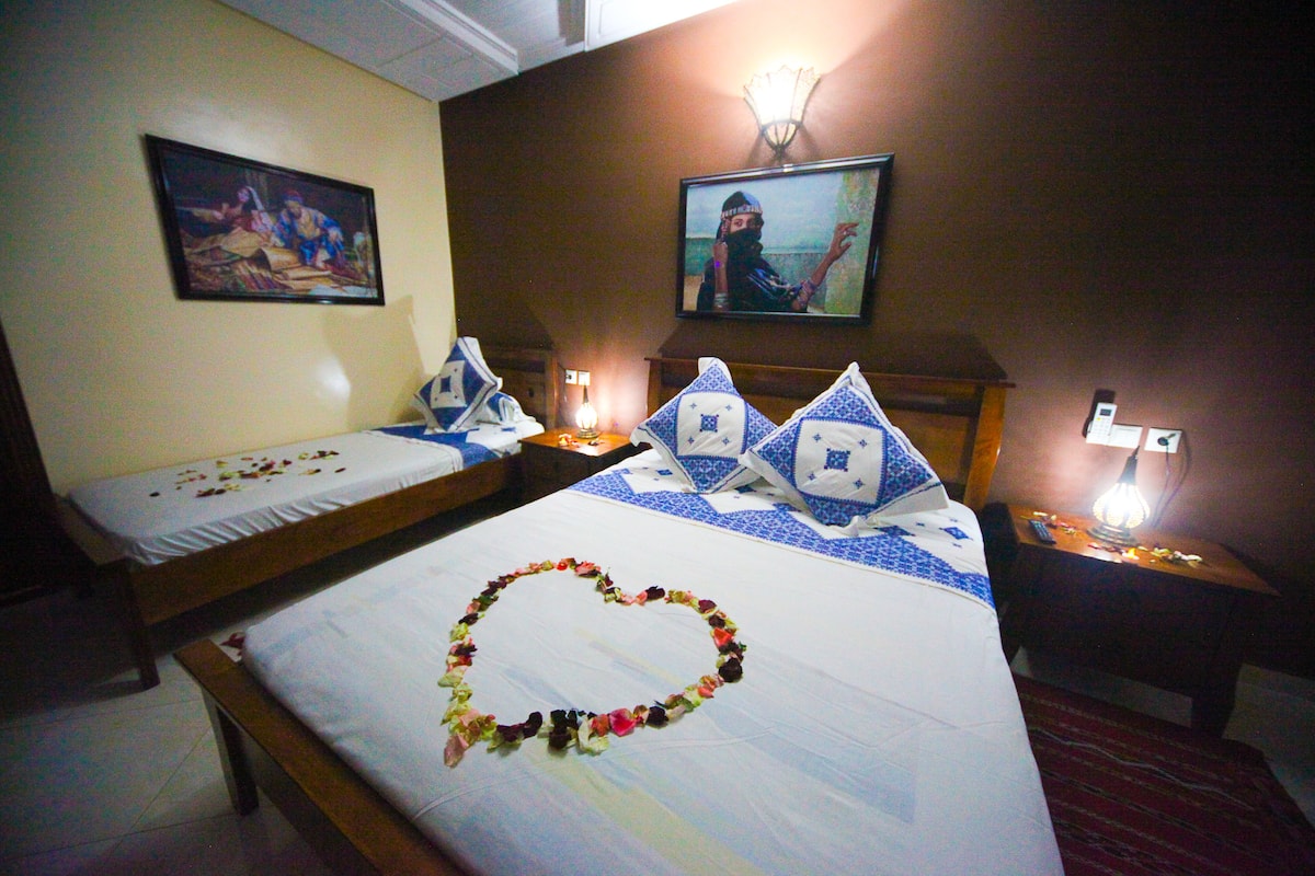 Een hotelkamer met twee bedden, waarvan er één voorzien is van een bloemstuk in de vorm van een hart, en een televisie aan de muur.