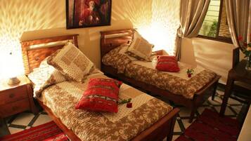 Quarto com duas camas de madeira, cada uma com roupa de cama estampada e almofadas, uma mesa de cabeceira de madeira, um quadro emoldurado na parede e uma janela com cortinas.