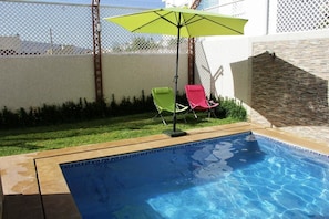 A swimming pool with two lounge chairs and a green umbrella.