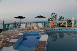 A pool area with lounge chairs and umbrellas, a tiled deck, and a view of the sea. - La Source Hotel & Resort (Roche-à-Bateau)