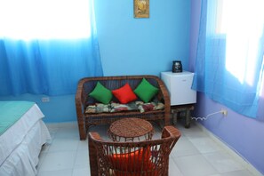 Una habitación con pared azul, un sofá de mimbre con cojines coloridos, una mesita redonda y un armario blanco.