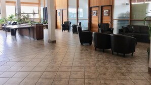 Een ruime lobby met een receptiebalie, verschillende zwarte leren stoelen, een houten balie en een betegelde vloer.