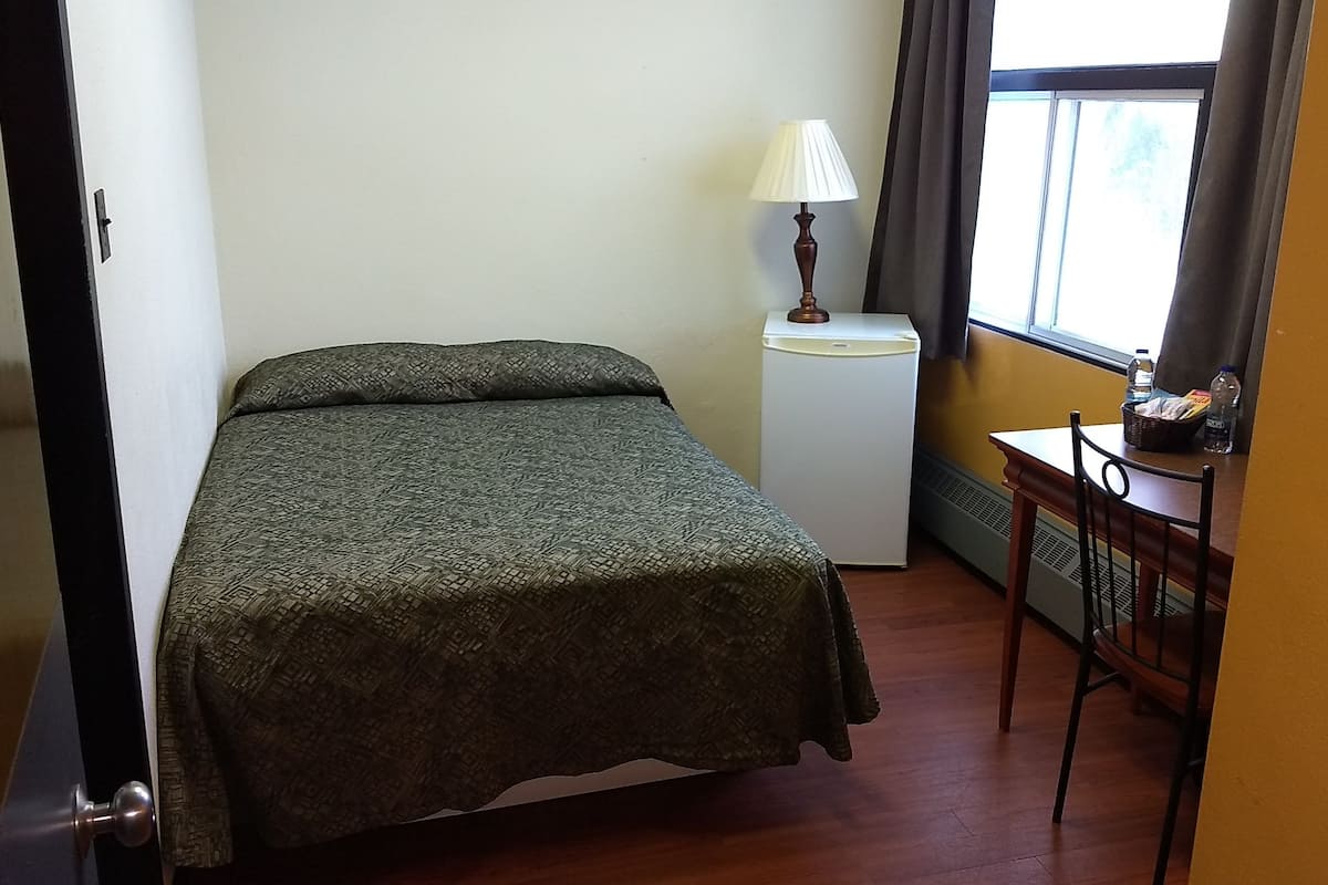 A bedroom with a bed, a small table with a lamp, and a window with curtains.