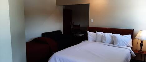 Una habitación de hotel con una cama grande, una mesita de noche de madera, una silla y un escritorio.