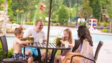 Un groupe de personnes est assis autour d’une table près d’une piscine, et profite de boissons et d’en-cas.