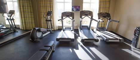 A gym with treadmills, elliptical machines, and a bench.