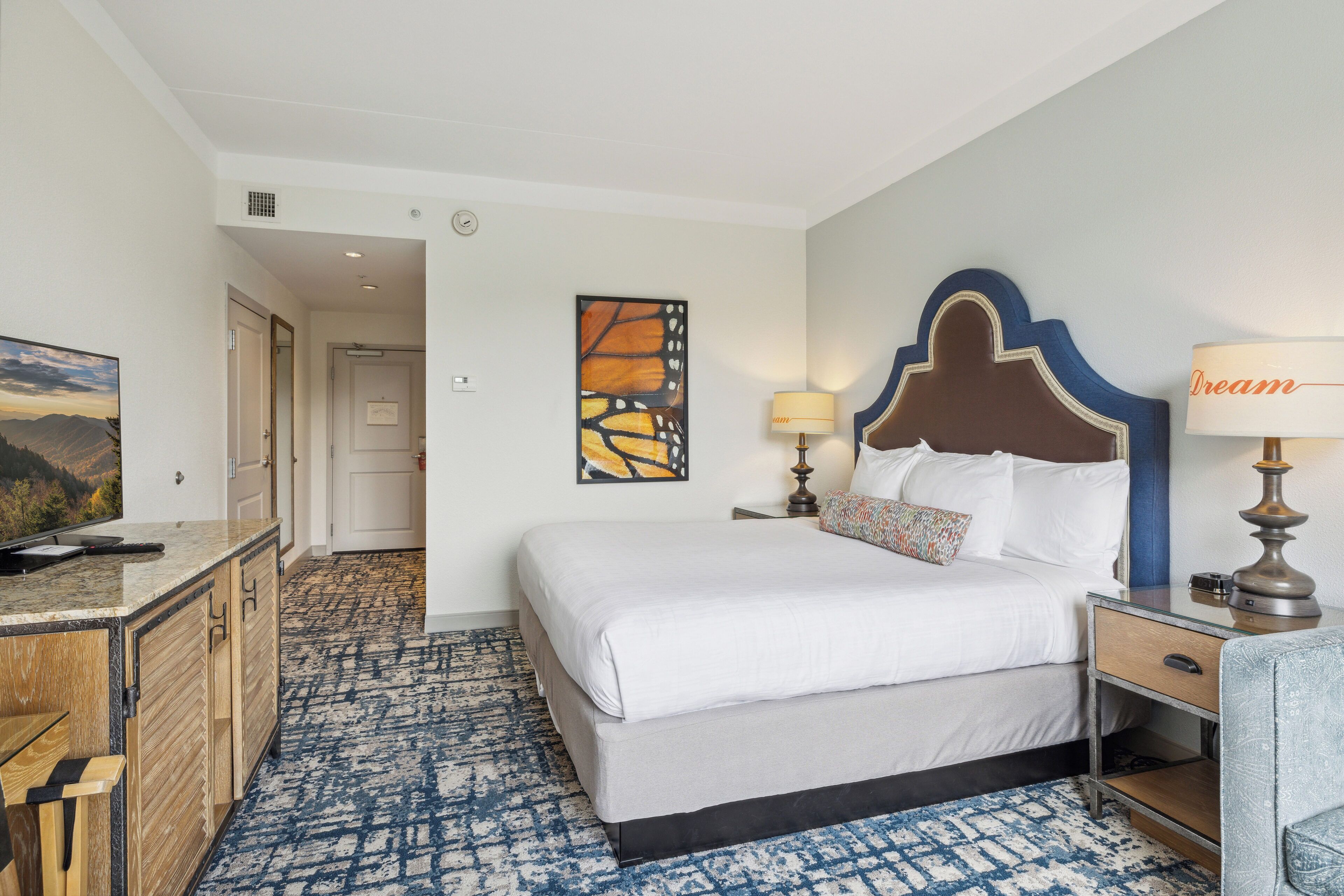 A hotel room with a bed, bedside table, lamp, and a painting on the wall.