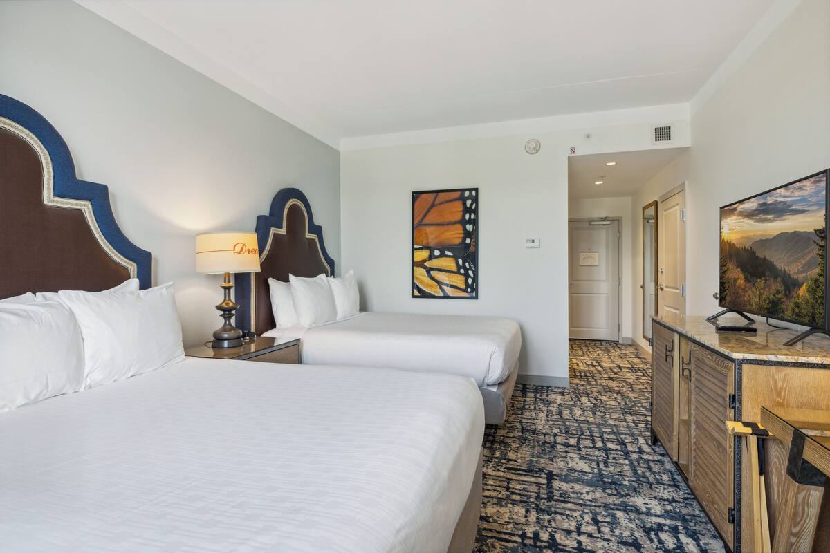 A hotel room with two beds, a desk, a lamp, and artwork on the walls.