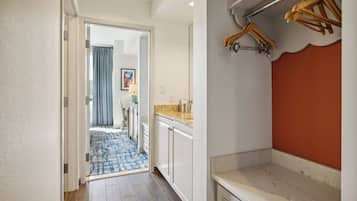 A hallway with a wooden floor, white walls, and a kitchen area with a countertop and cabinets.