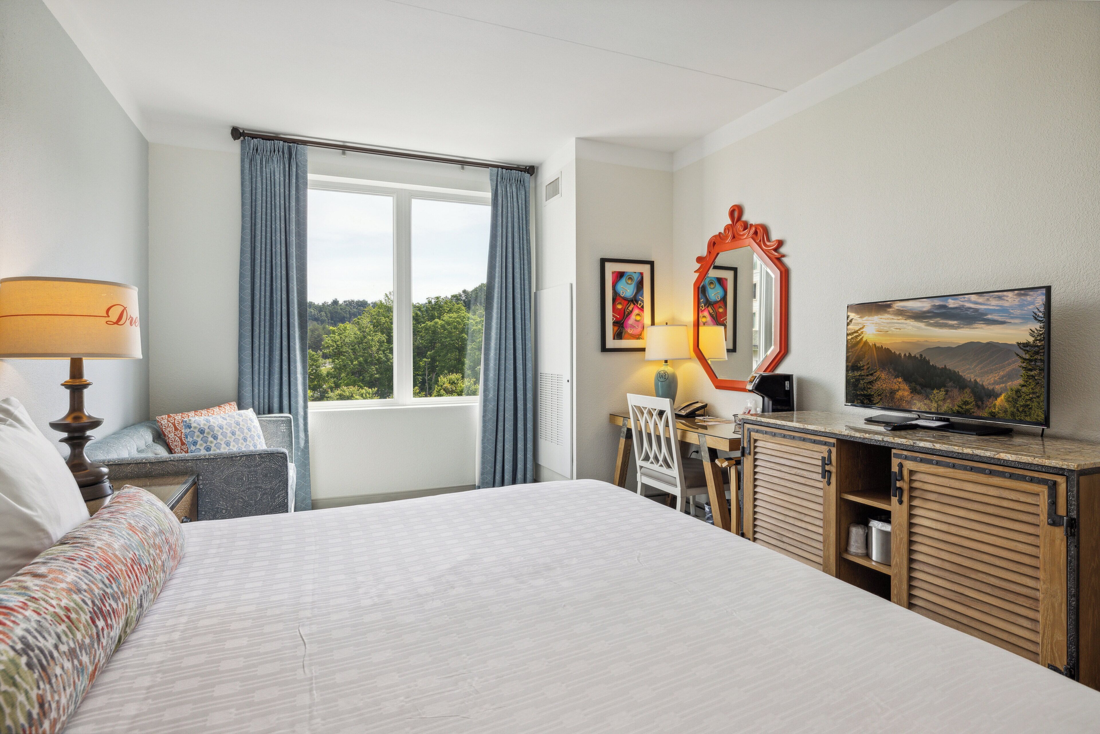 A hotel room with a large bed, a desk with a chair, a television, and a window with curtains.