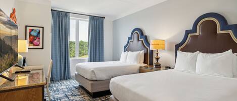 Een hotelkamer met twee bedden, een bureau met lamp, een televisie en een raam met gordijnen.