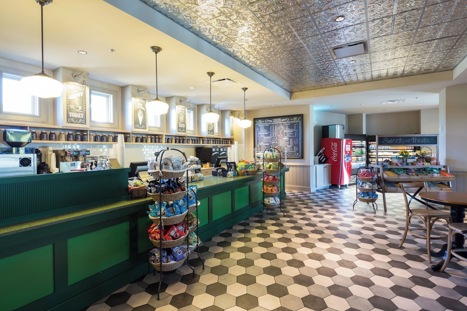 Una cafetería con mostrador verde, suelo de patrón hexagonal y un cartel de menú.