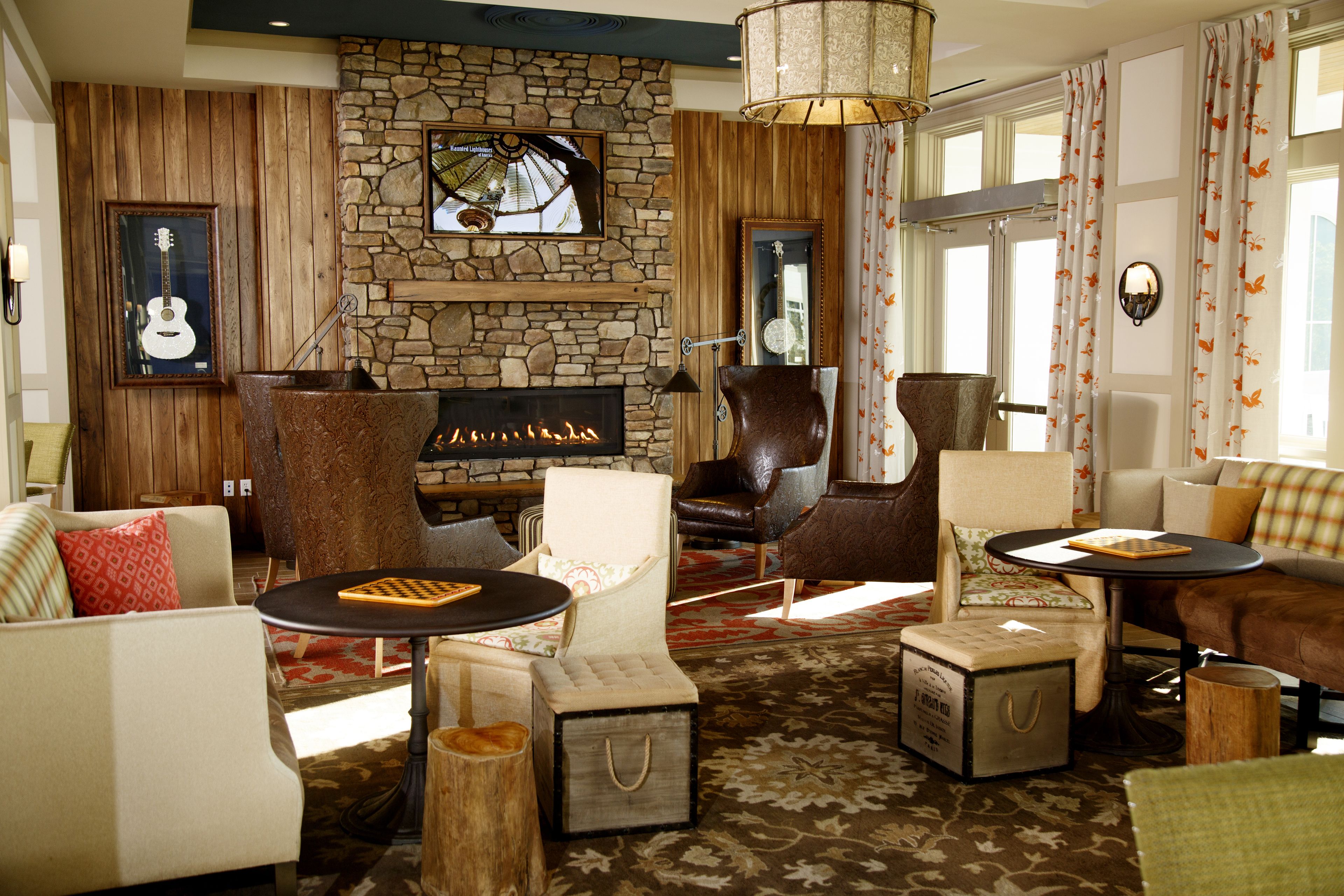 A cozy living room with a stone fireplace, comfortable seating, and a large window with curtains.
