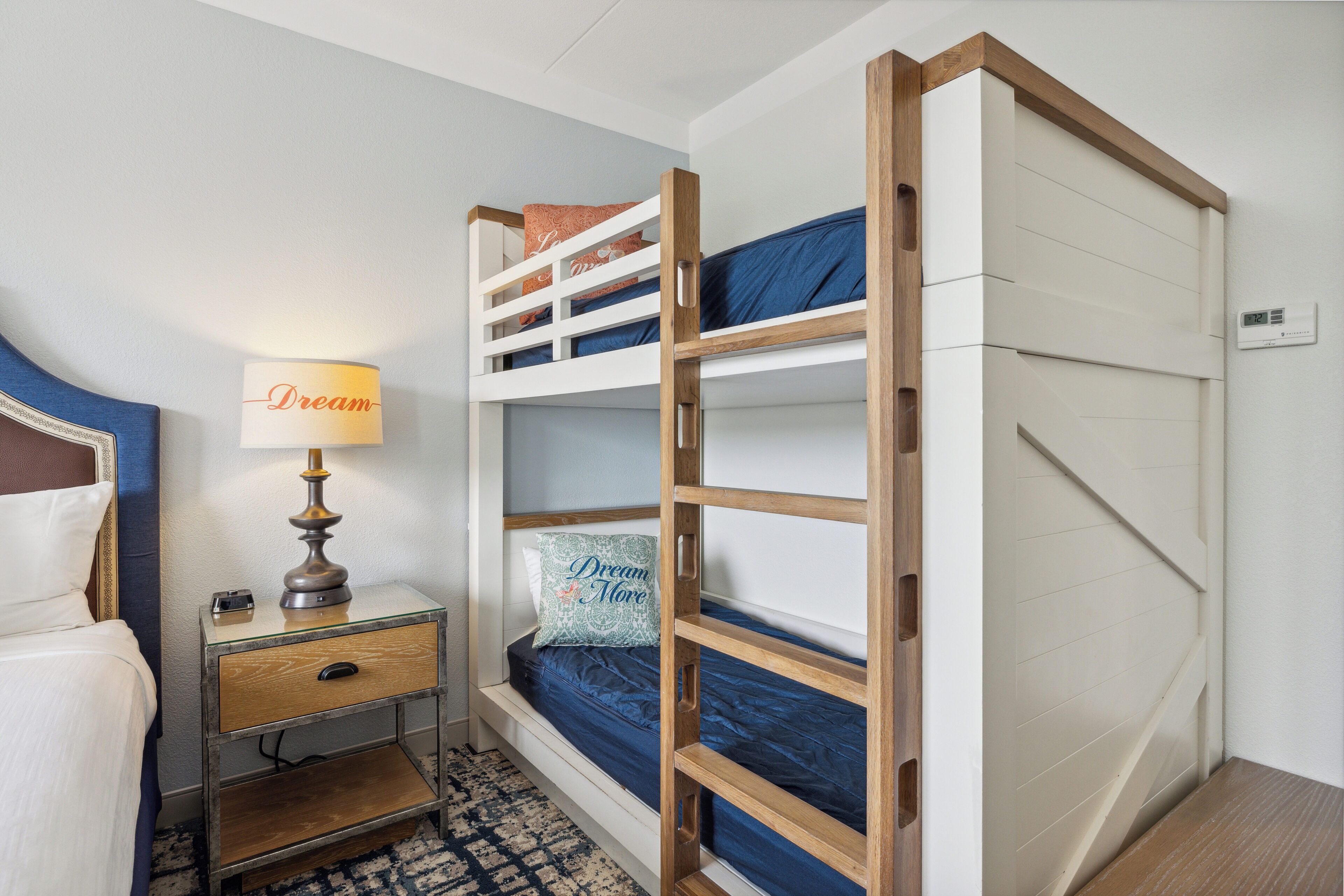 Een stapelbed met een houten trap, een nachtkastje met een lamp en een nachtkastje.