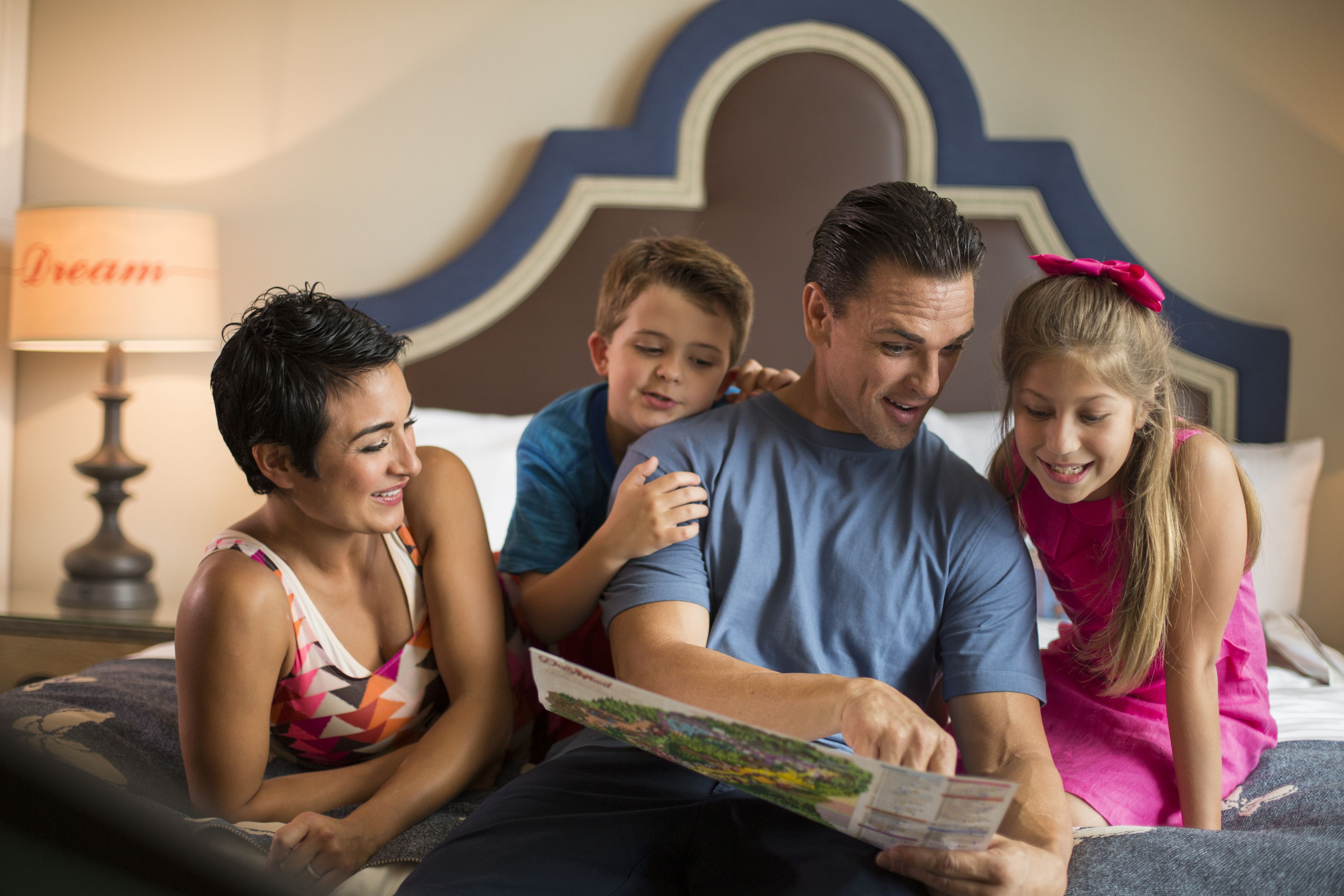 A family of four on a bed with a headboard, a lamp, and a sign that reads "Dream" in the background.