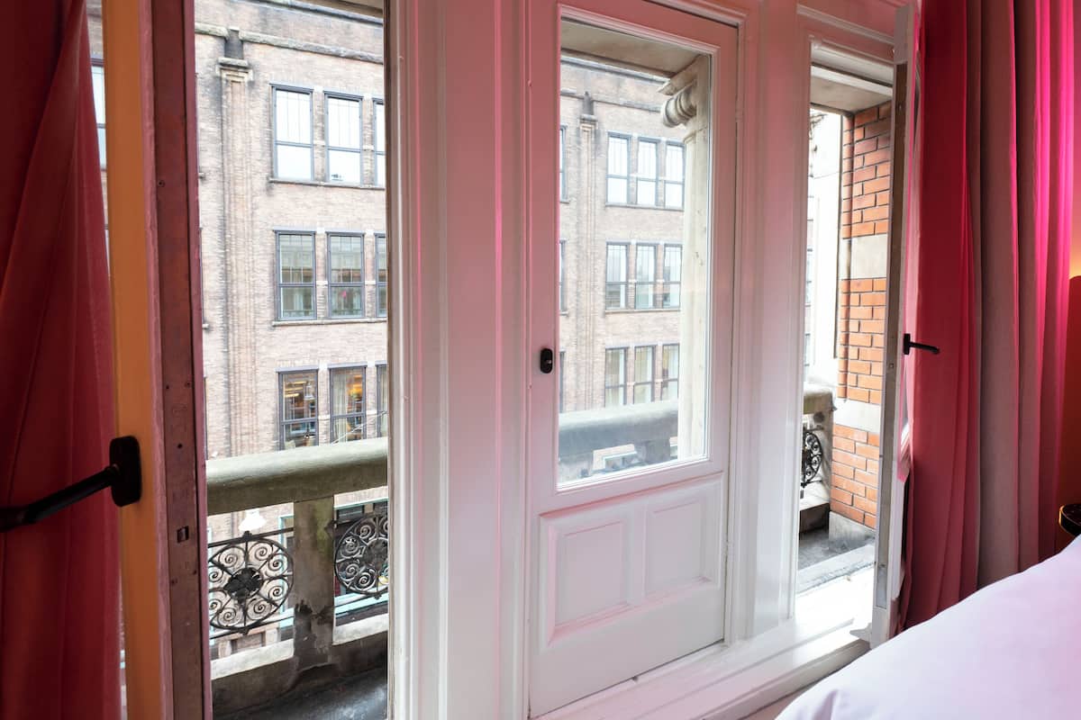 Una habitación con puerta blanca, cortinas rosadas y vistas a un edificio de ladrillo con varias ventanas.