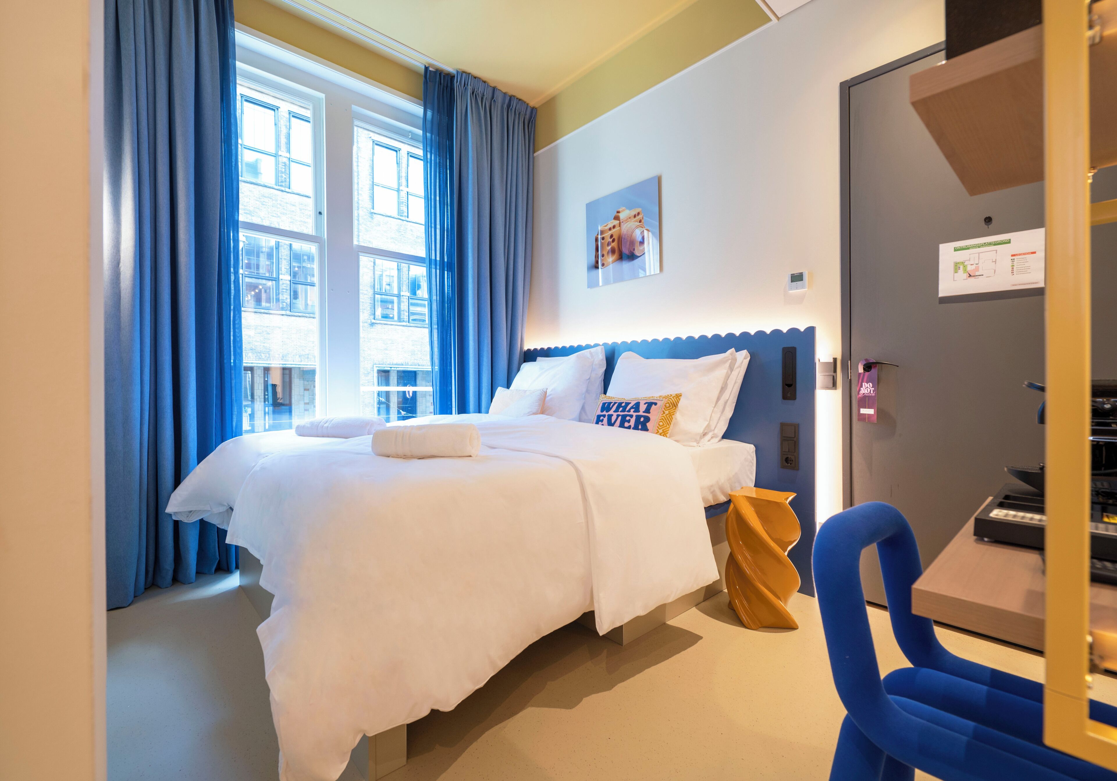 Habitación de hotel con una cama grande, un escritorio, una silla y vistas de la ciudad a través de la ventana.