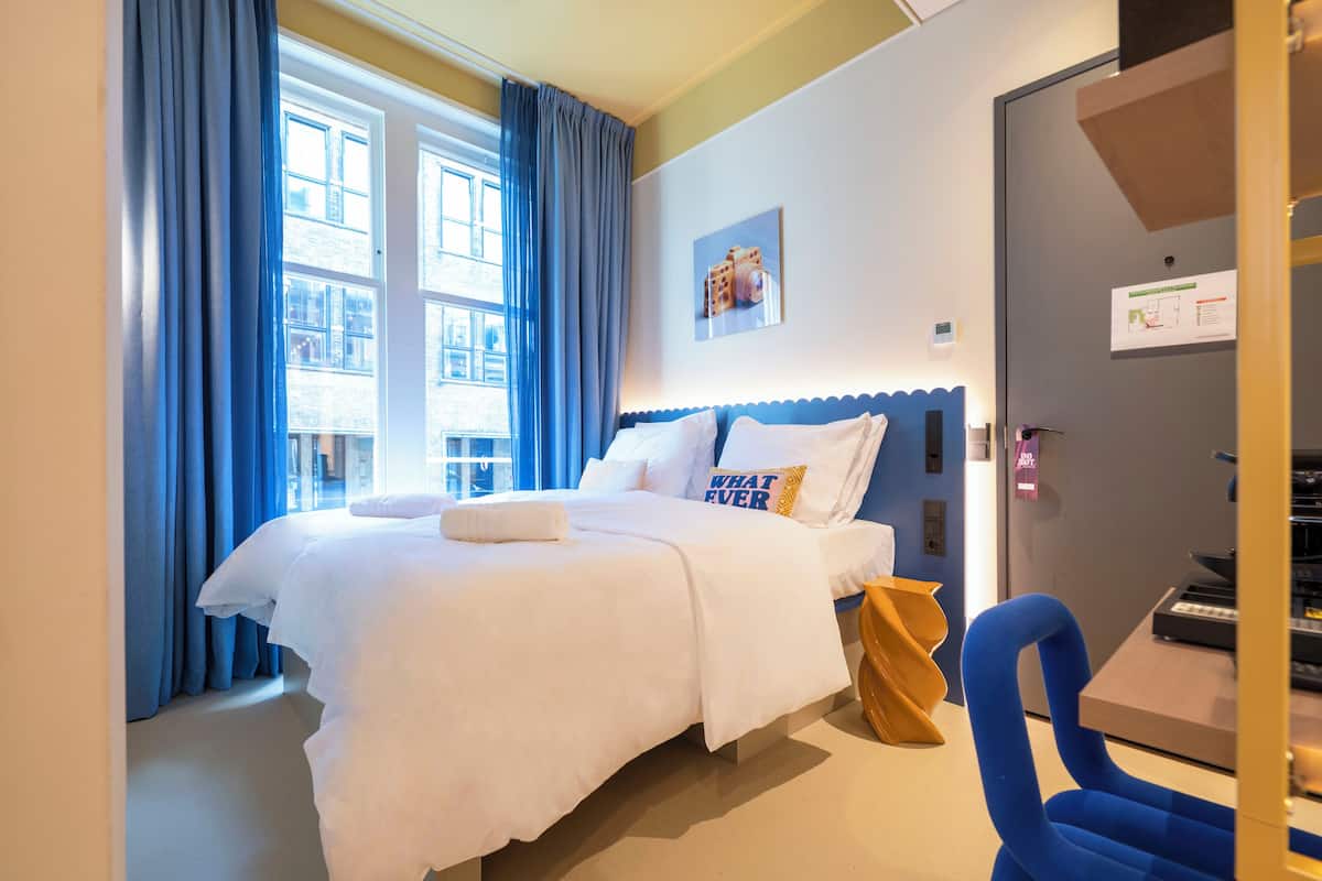 Habitación de hotel con una cama grande, un escritorio, una silla y vistas de la ciudad a través de la ventana.
