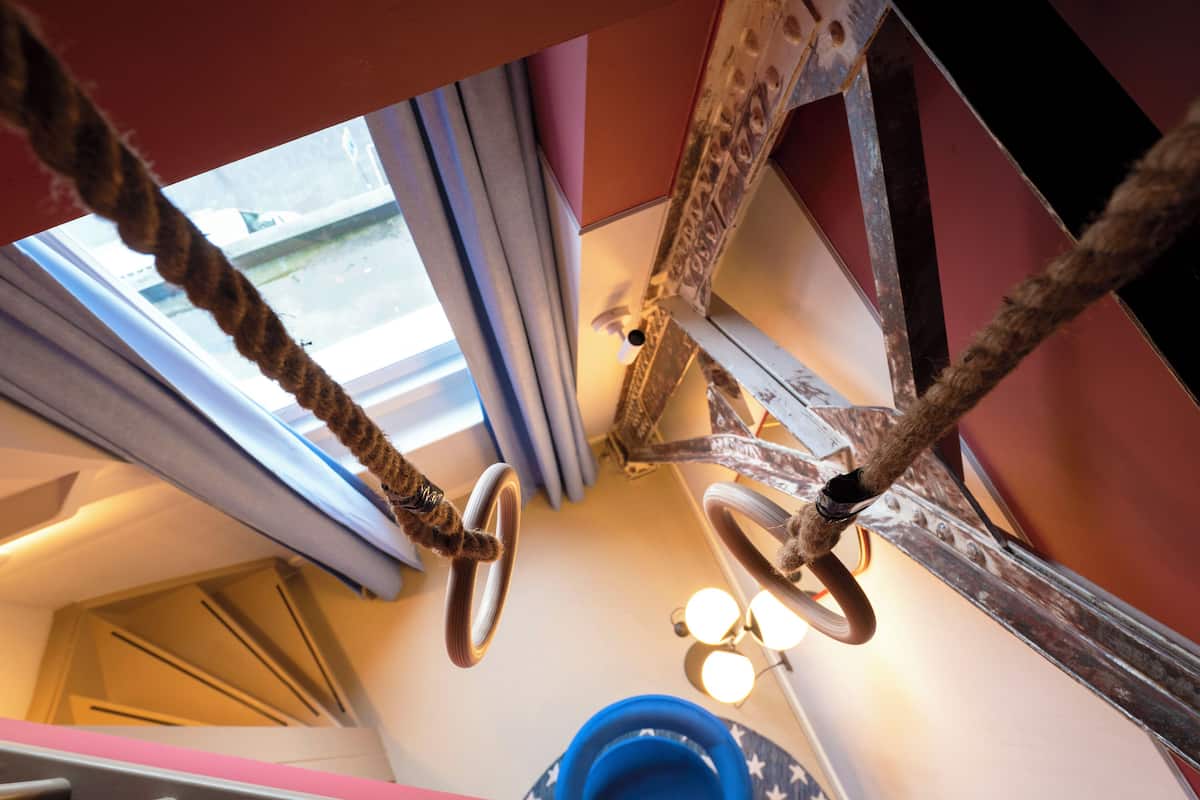 Una habitación con ventana, cortinas, estructura metálica y un objeto azul en el suelo.