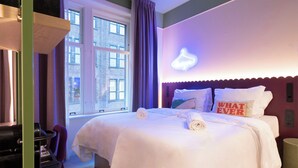 Una habitación de hotel con cama, ventana, un letrero de neón y una cafetera.