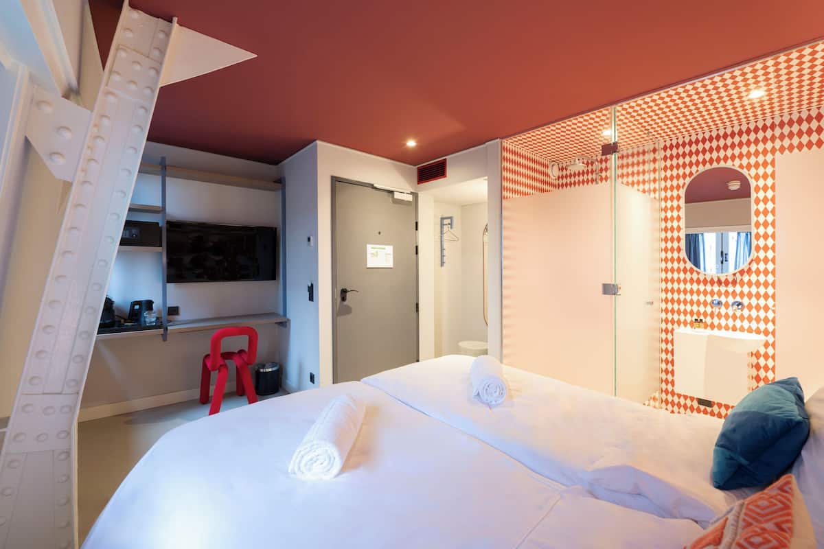 Habitación de hotel con cama, escritorio, silla, espejo y una silla roja.