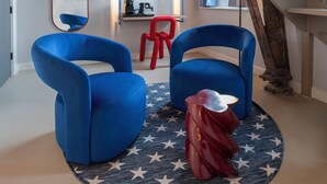Una sala de estar moderna con un sofá azul, una butaca roja, un tapete estampado con estrellas, una escalera de madera y una pared espejada.