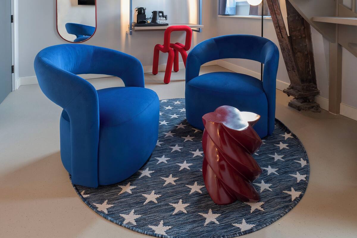 Un interior moderno con una escalera, dos sillas azules, una silla roja, una alfombra redonda con estrellas y un espejo.