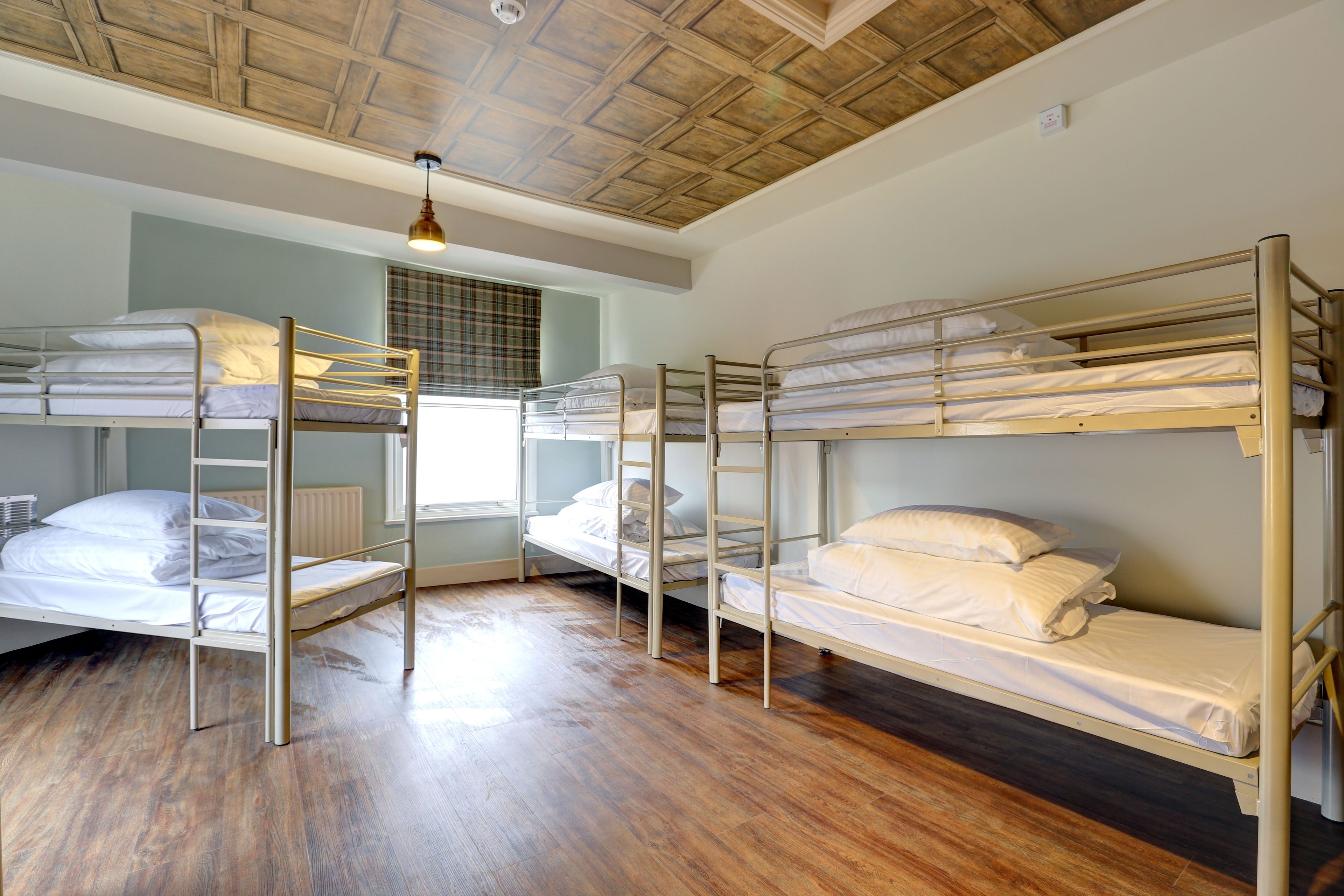 A dormitory room with bunk beds, wooden flooring, and a ceiling with a wooden panel design.
