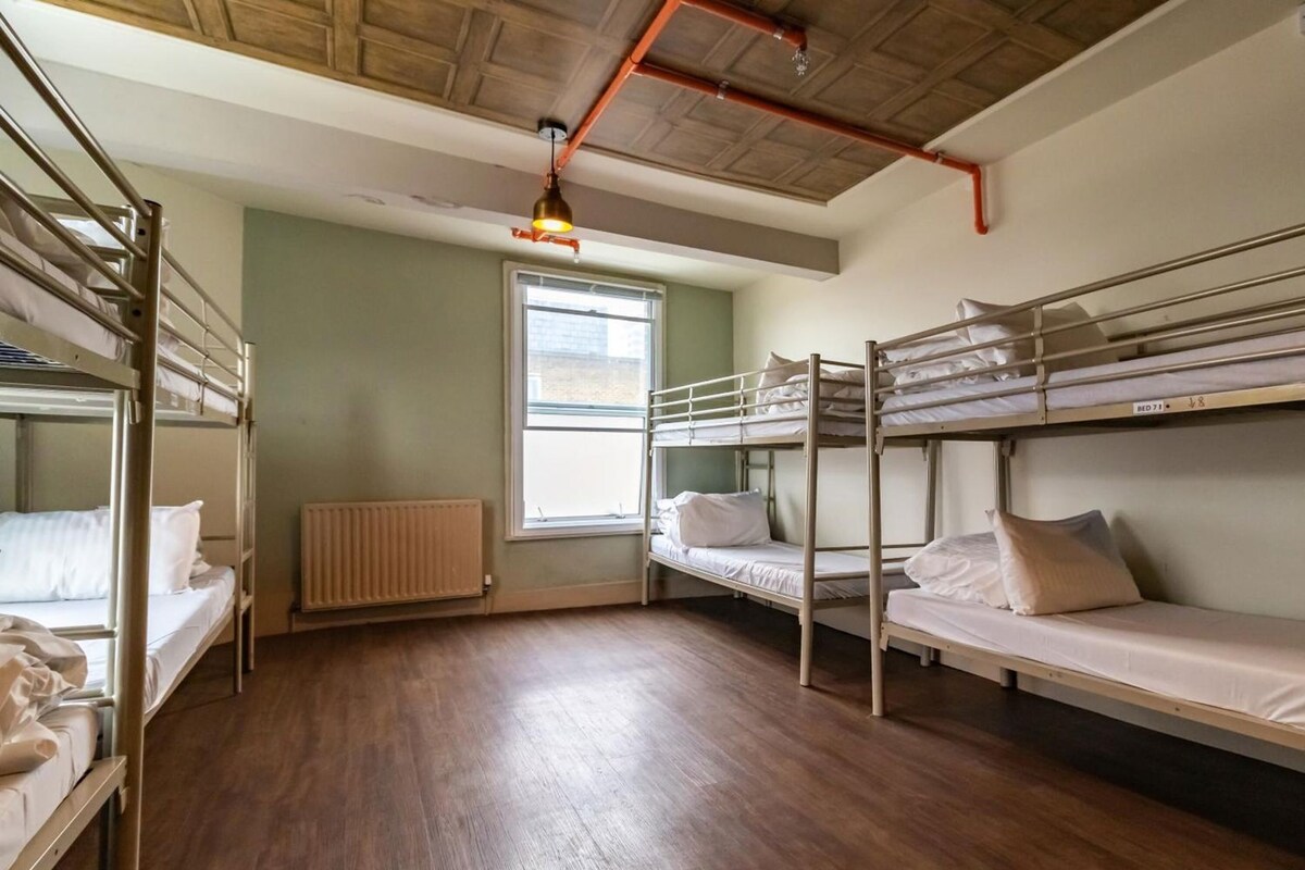 A dormitory room with bunk beds, a radiator, a window, and a wooden floor.