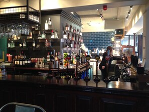 A bar area with shelves of liquor bottles, a bartender, and a counter with glasses and bottles. - Publove @ Exmouth Arms Euston (London)