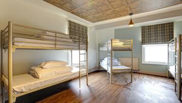 A room with bunk beds, wooden flooring, a ceiling with a wooden panel design, and a window with blinds.