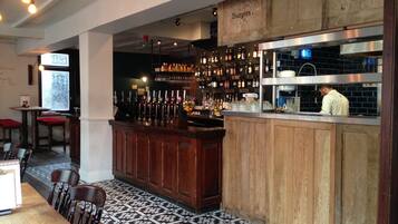 A bar area with a wooden counter, bar stools, and a tiled floor.