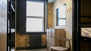 A dormitory room with bunk beds, a radiator, a window, a wooden chair, and a cabinet with numbered drawers. - Publove @ Exmouth Arms Euston (London)