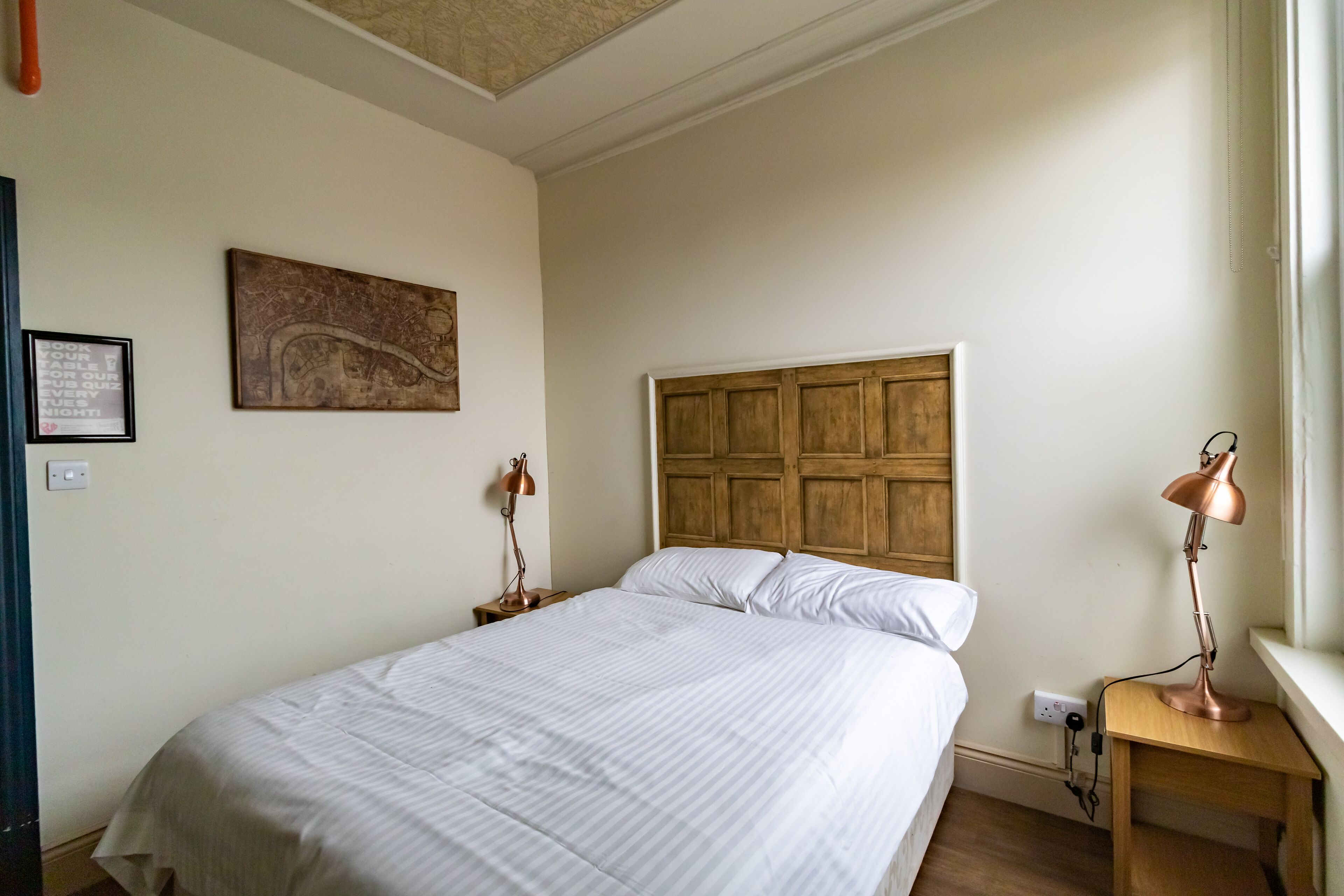 Una cama bien hecha con cabecera de madera, un mapa colgado en la pared y dos lámparas de noche.